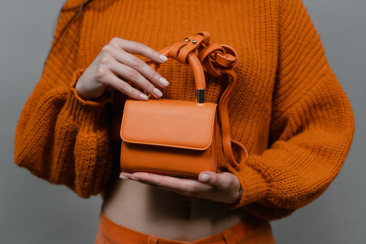 The Art of Drawing Readers In: Your attractive post title goes here Woman holding an orange leather mini handbag against an orange sweater in a studio setting.